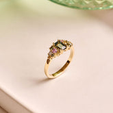 Handmade cluster engagement ring in 9ct yellow gold with a central emerald-cut green sapphire, surrounded by green, yellow, and pink sapphires and two natural diamonds in a floral-inspired design.