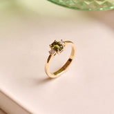 Handmade 9ct yellow gold trilogy ring featuring an emerald-cut green sapphire centre stone flanked by two round natural diamonds; elegant three-stone engagement ring design with timeless appeal.
