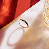 Handmade 9ct yellow gold wedding ring set with seven 2.5mm natural black diamonds; a modern, minimalist design perfect for unique wedding bands or alternative fine jewellery. Photographed on a red and white background and styled with a luxury whiskey glass.