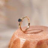 An emerald cut blue sapphire set in a yellow gold ring with hand engraved botanical details on the band