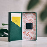 Open green box with floral patterned interior, yellow card, and black square engagement ring box on a light surface.