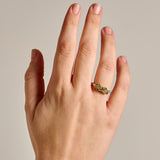 A close-up of a hand wearing the solid gold earth-toned Bouquet Ring with natural diamonds, set against a plain light gray background.