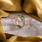 Handmade cluster engagement ring in 9ct yellow gold with a central emerald-cut green sapphire, surrounded by green, yellow, and pink sapphires and two natural diamonds in a floral-inspired design.