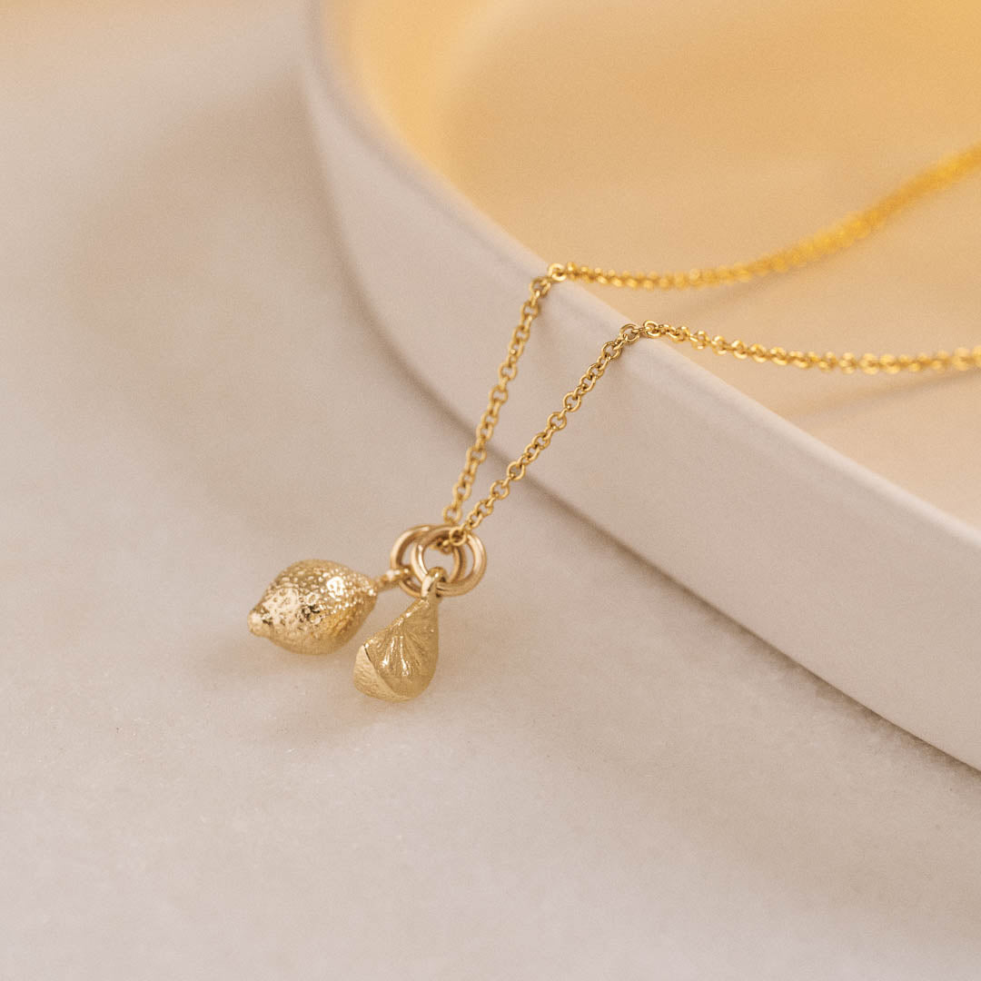 A miniature yellow gold Lemon charm and Citrus Wedge charm on a yellow gold rolo chain.