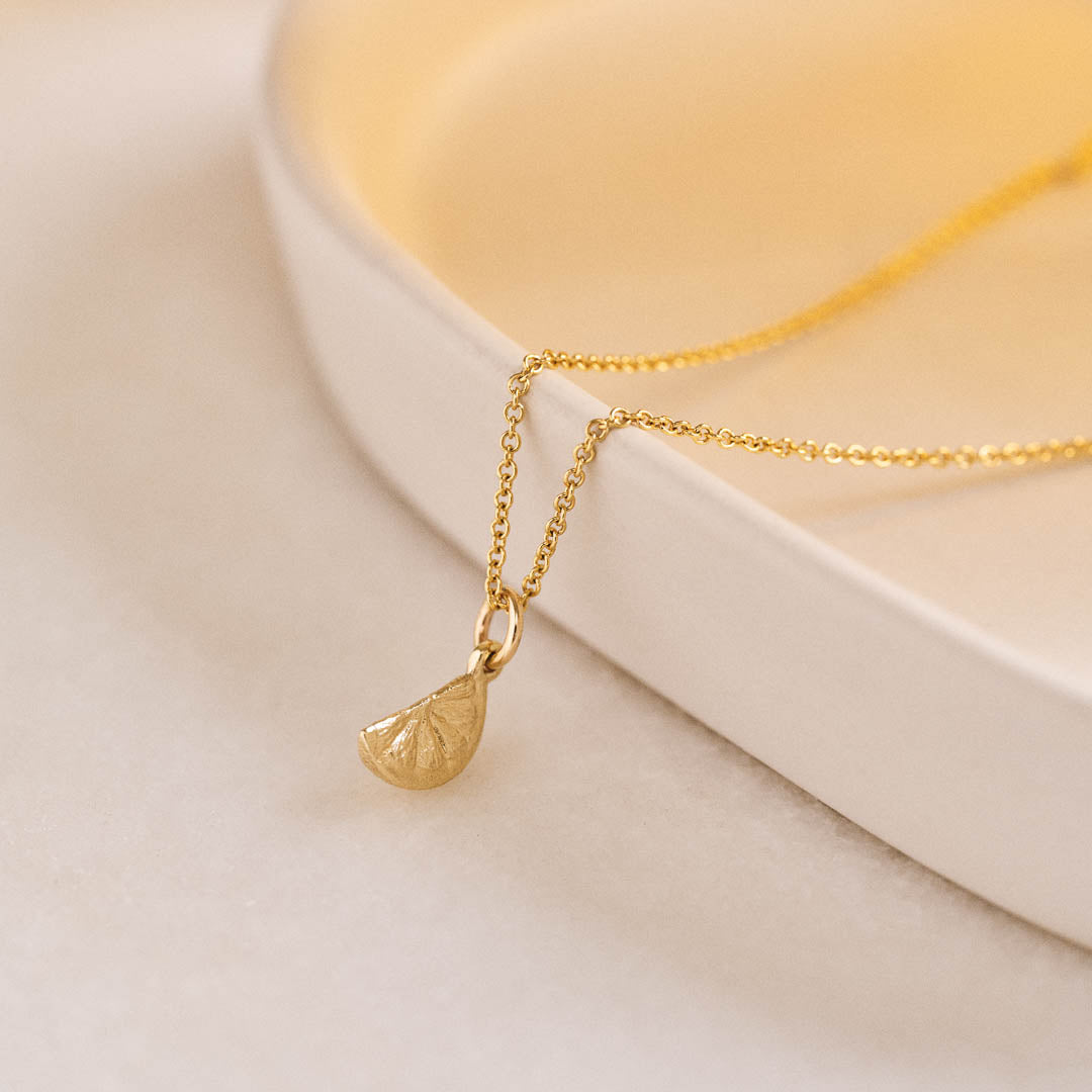 A miniature yellow gold citrus wedge jewellery charm on a yellow gold rolo chain.