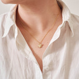 A miniature yellow gold frog jewellery charm on a yellow gold rolo chain. Photographed being worn.