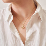A yellow gold pendant featuring leaves and lemon blossom flowers on a yellow gold curb chain being worn.