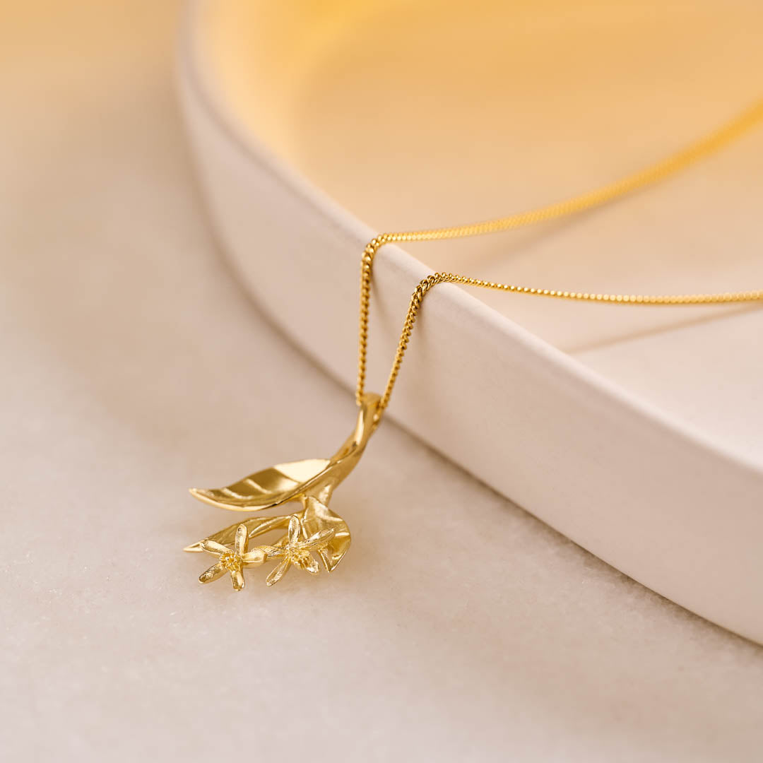 A yellow gold pendant featuring leaves and lemon blossom flowers on a yellow gold curb chain.