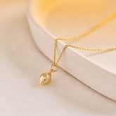 A miniature lemon jewellery charm in yellow gold, photographed on a yellow gold rolo chain.