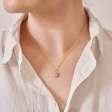 A miniature pear jewellery charm in yellow gold, on a yellow gold rolo chain, photographed being worn.