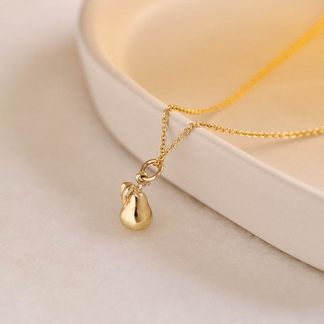 A miniature pear jewellery charm in yellow gold, photographed on a yellow gold rolo chain.