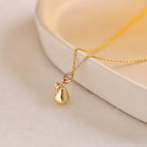 A miniature pear jewellery charm in yellow gold, photographed on a yellow gold rolo chain.