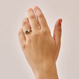 Handmade 14ct yellow gold engagement ring featuring a round green sapphire centre stone flanked by two natural round diamonds; luxury heirloom-quality design perfect for weddings or special occasions; photographed on a hand with a plain background.