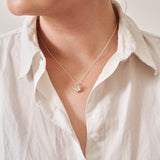 A miniature silver watering can jewellery charm on a silver rolo chain. Photographed being worn.