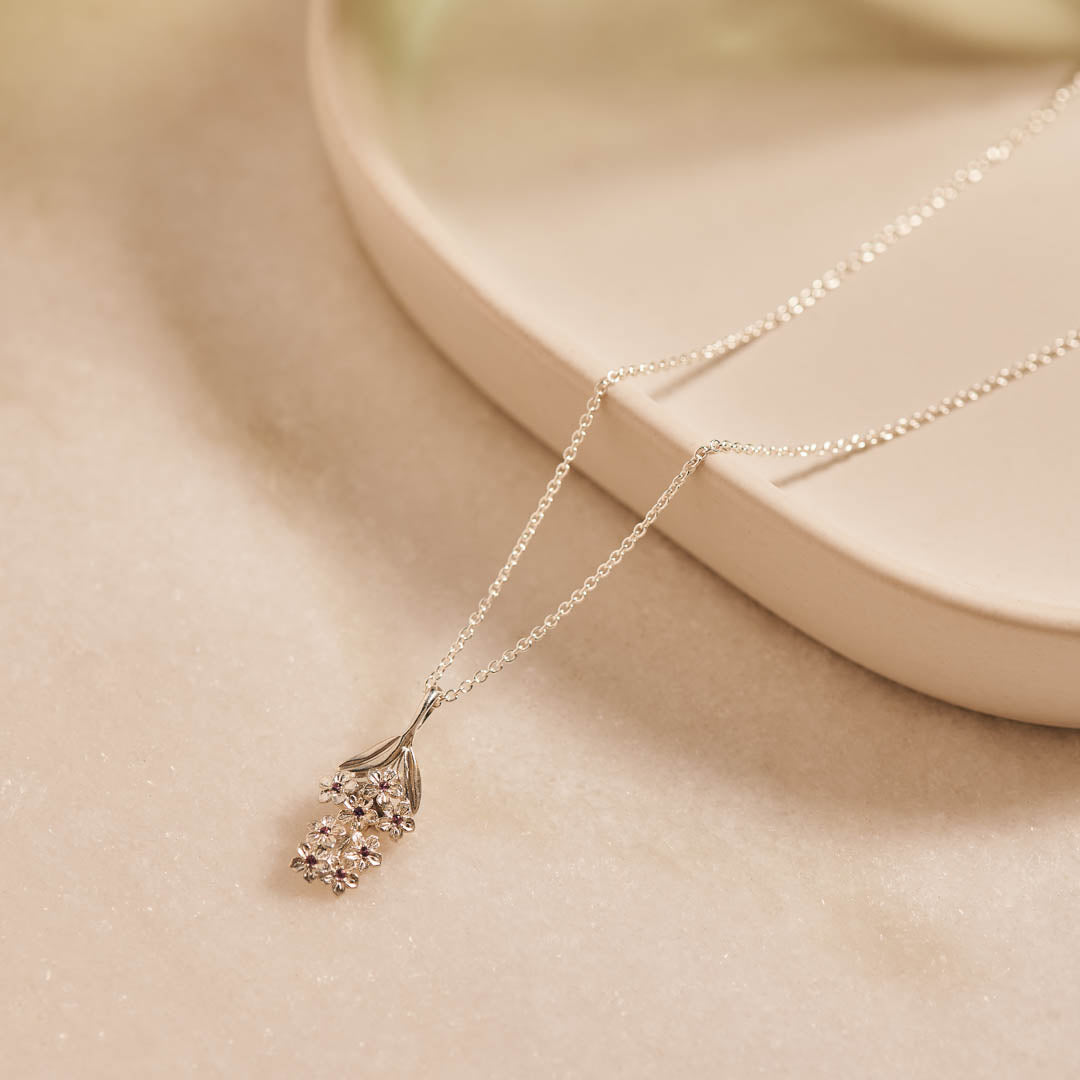 Forget-Me-Not flower inspired pendant with leaf detail, manufactured in sterling silver, set with lilac sapphires, and on a sterling silver rolo chain