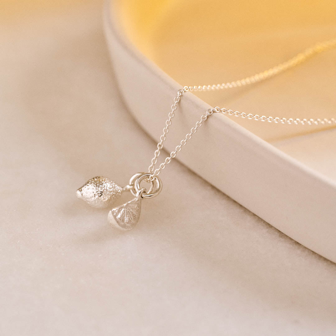 A miniature silver Lemon charm and Citrus Wedge charm on a silver rolo chain.