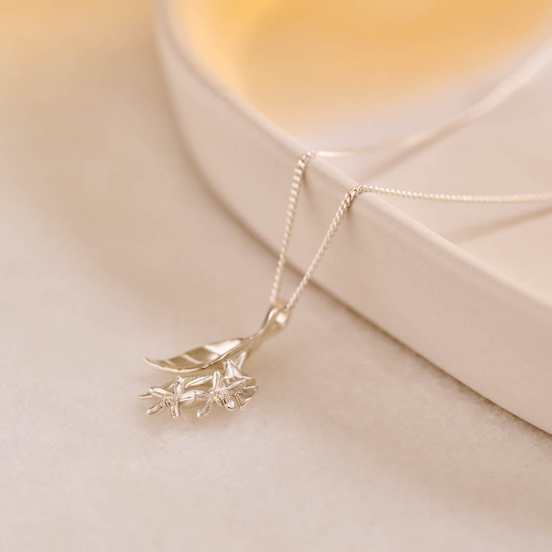 A silver pendant featuring leaves and lemon blossom flowers on a silver curb chain.