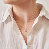 A miniature lemon jewellery charm in silver on a silver rolo chain, photographed being worn.