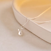 A miniature pear jewellery charm in silver, photographed on a silver rolo chain.