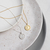 Sterling silver and yellow gold disc pendants with wreath borders and an engraved initial.