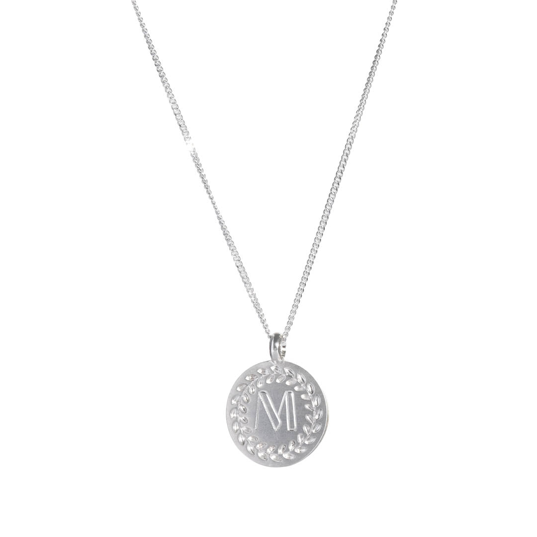 Sterling silver disc pendant with wreath border and an engraved initial.