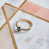A vibrant blue green Tourmaline set in a classic six claw setting, accentuated with black diamonds set into the yellow gold band