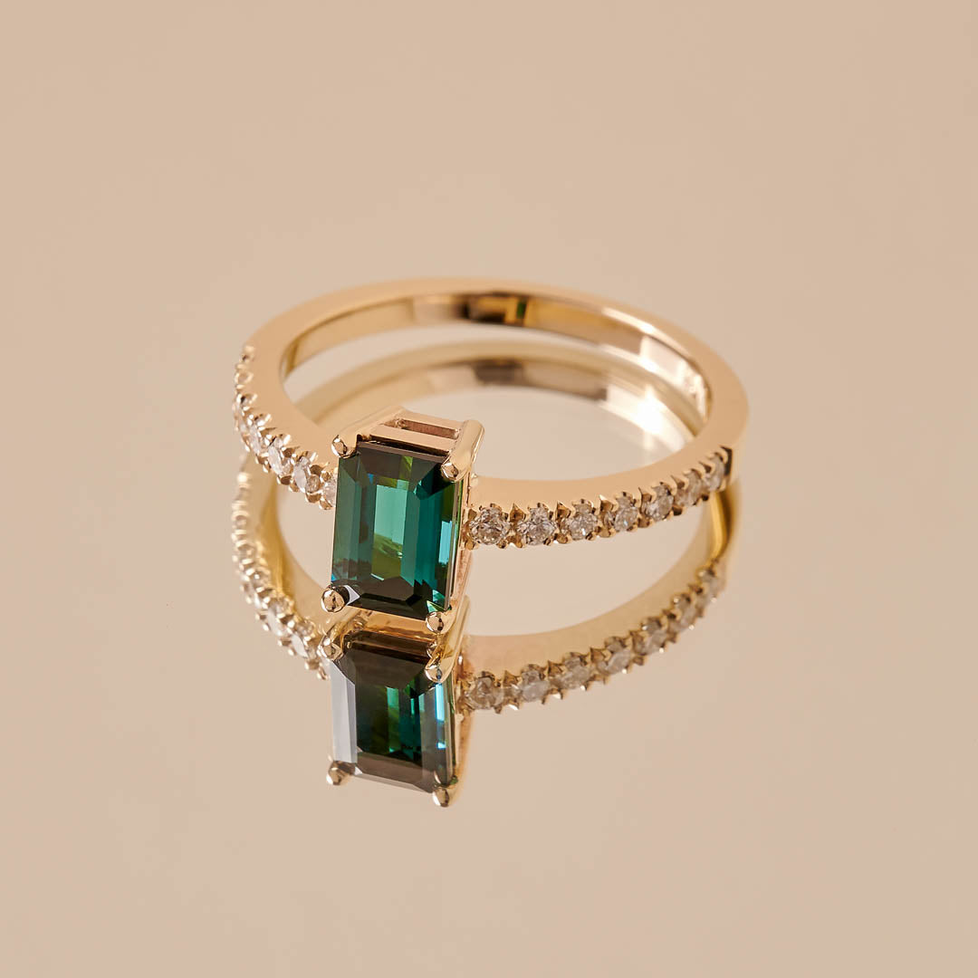 A teal rectangular cut tourmaline set in a yellow gold ring with 7 1.5mm diamonds set into the band on either side