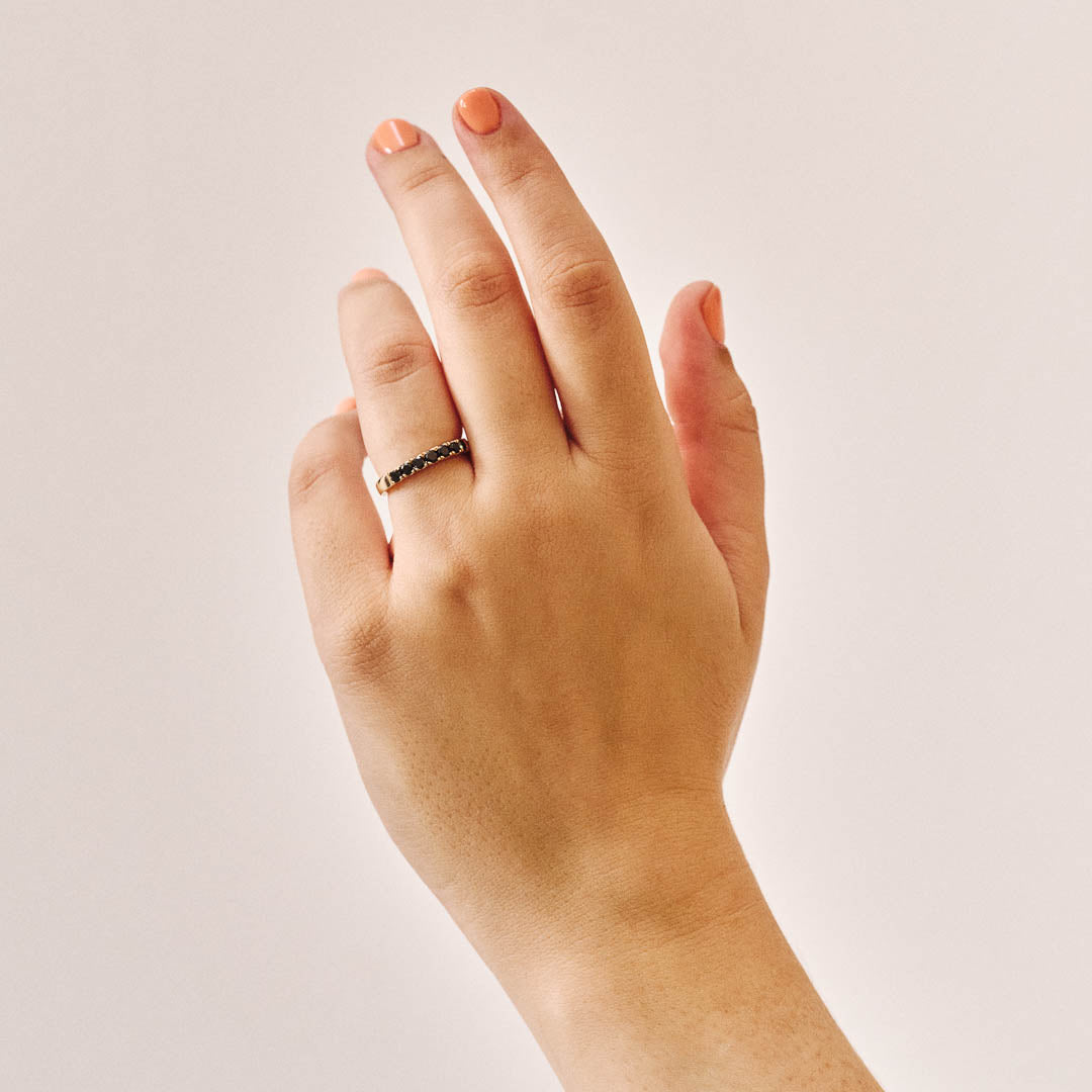 Handmade 9ct yellow gold wedding ring set with seven 2.5mm natural black diamonds; a modern, minimalist design perfect for unique wedding bands or alternative fine jewellery. Photographed on a hand with a plain background.