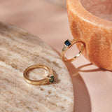 An emerald cut blue sapphire and teal round sapphire set in yellow gold rings with hand engraved botanical details on the band