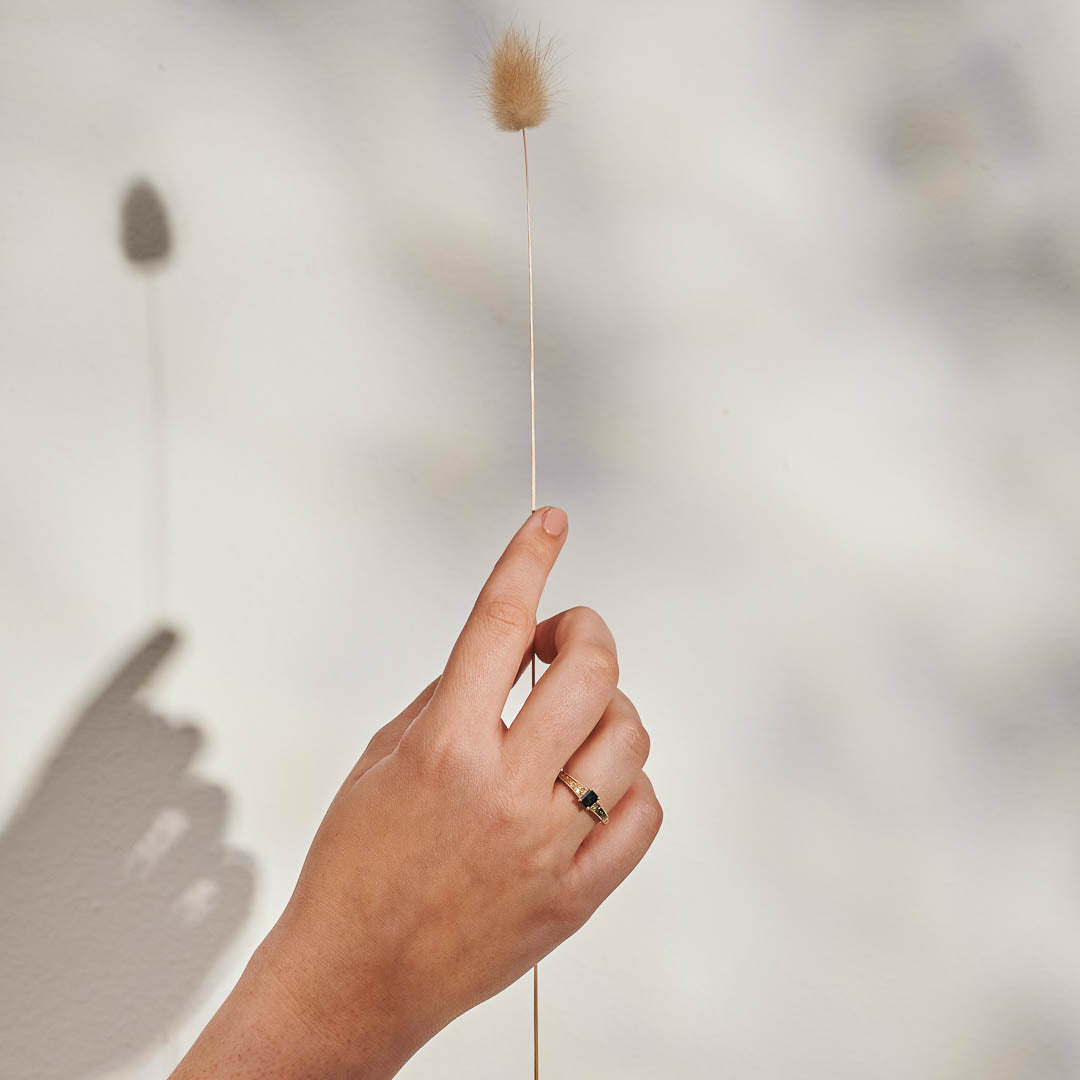 An emerald cut blue sapphire set in a yellow gold ring with hand engraved botanical details on the band - photographed on a hand.