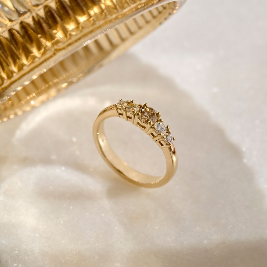 A solid gold ring with a central fancy brown diamond, known as a champagne diamond, flanked by four colourless natural diamonds tapering down in size all set in four claw settings. 
