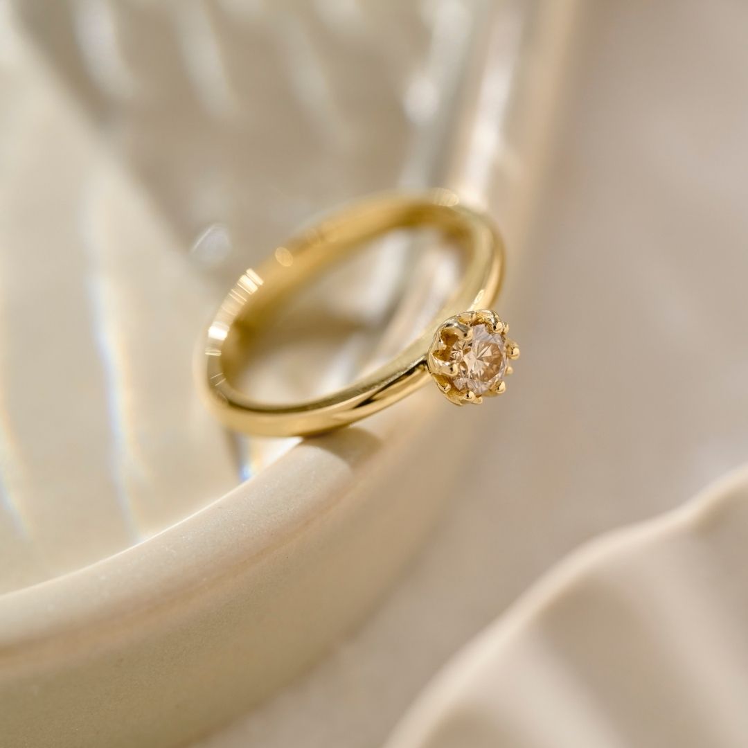 A solid yellow gold Botanica Protea Ring set with a cognac diamond in a six claw protea setting resting on a cream ceramic bowl. 