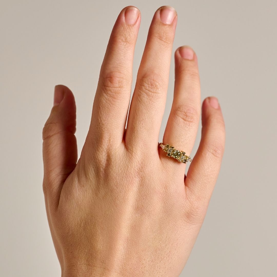 A close-up of a hand wearing the solid gold earth-toned Bouquet Ring with natural diamonds, set against a plain light gray background.