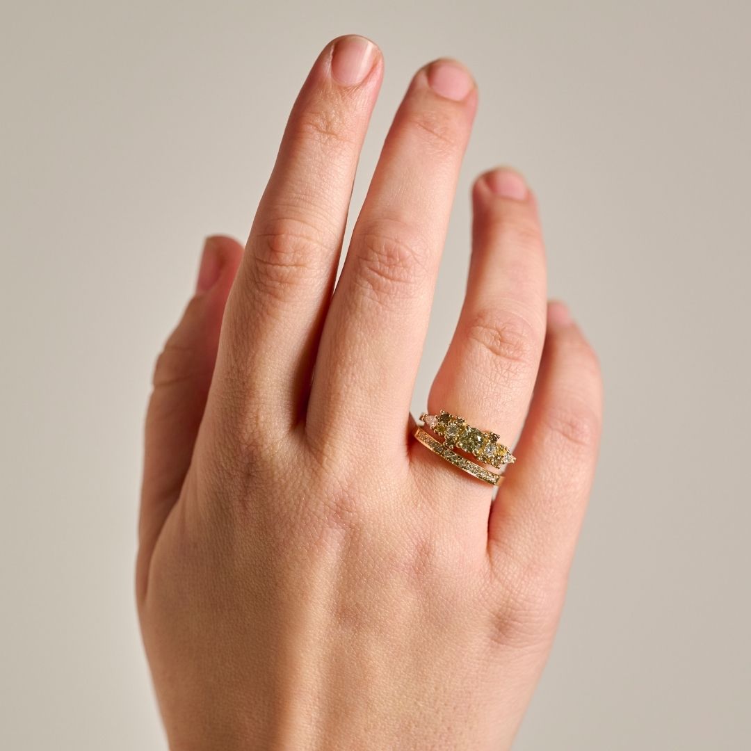 A close-up of a hand wearing the solid gold earth-toned Bouquet Ring with natural diamonds paired with the solid gold and natural diamond pave wedding ring, set against a plain light gray background.