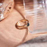 A round teal sapphire set in a yellow gold ring with hand engraved botanical details on the band