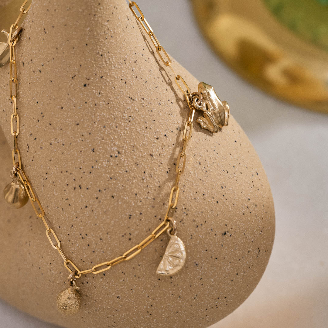 Yellow gold miniature frog, citrus wedge, lemon, pear, and leaf jewellery charms on a yellow gold paper clip chain.
