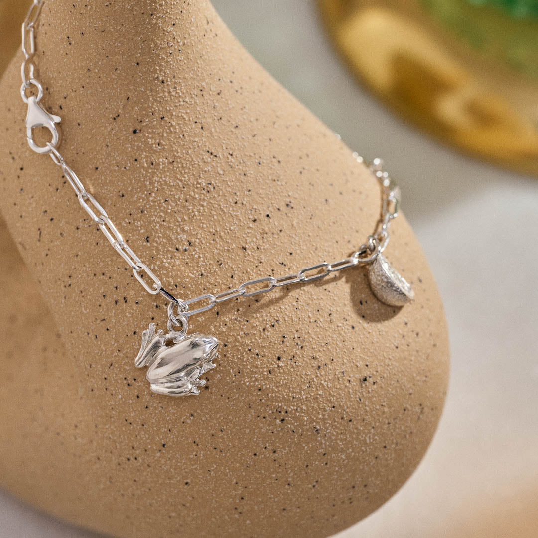 A silver miniature frog and citrus wedge jewellery charm on a silver paper clip chain.