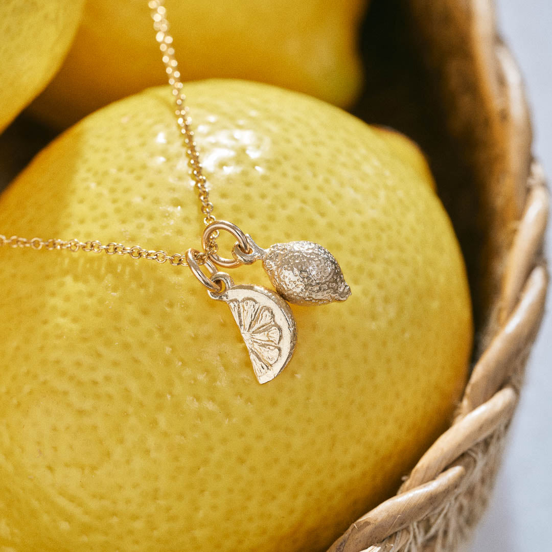 A miniature yellow gold Lemon charm and Citrus Wedge charm on a yellow gold rolo chain.