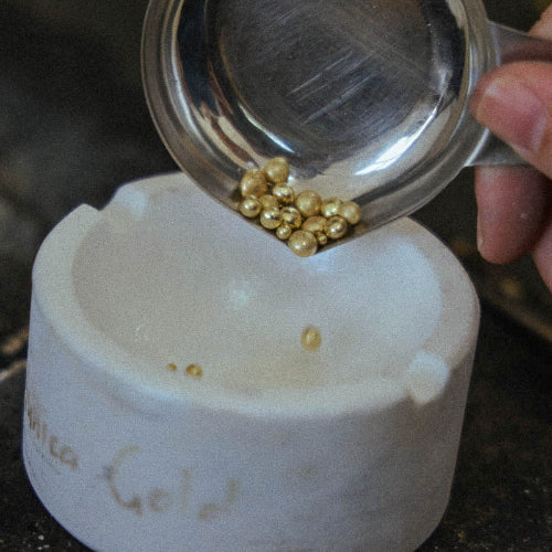 Gold granules being poured from a metal scoop into a crucible