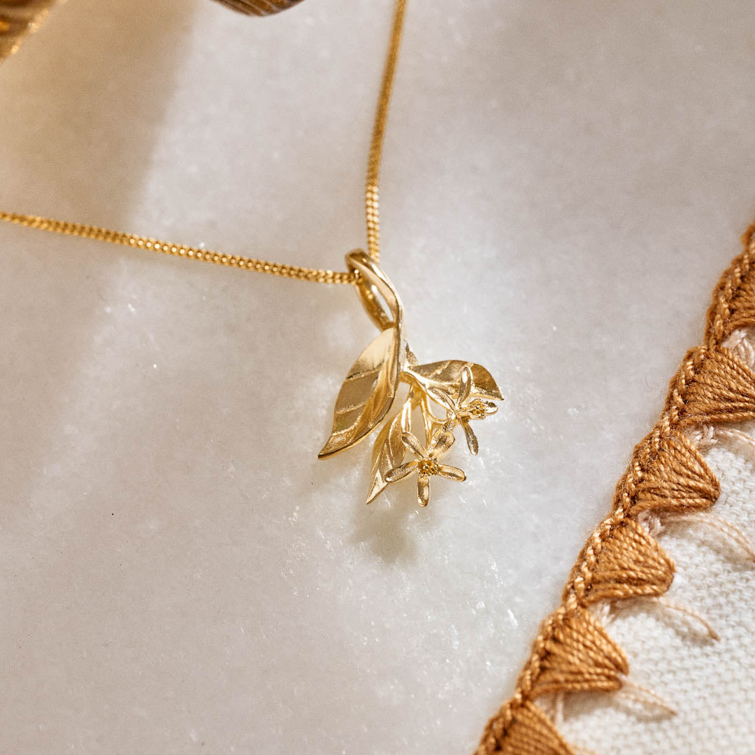 A yellow gold pendant featuring leaves and lemon blossom flowers on a yellow gold curb chain.