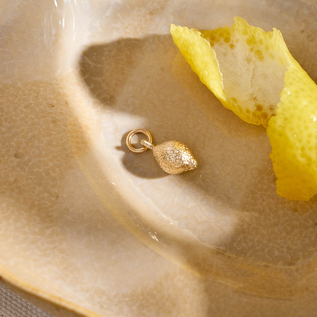 A miniature lemon jewellery charm in yellow gold.