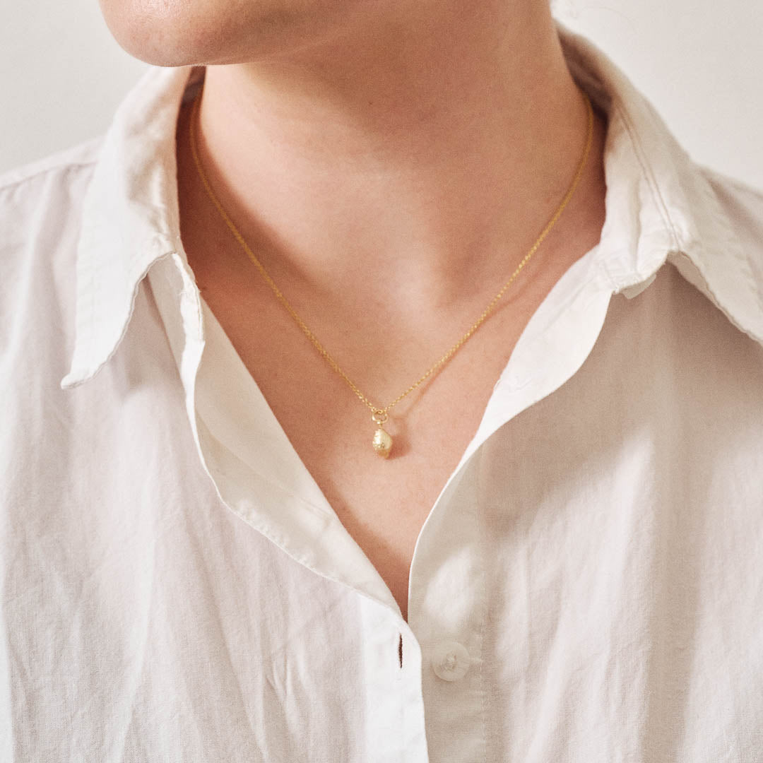 A miniature lemon jewellery charm in yellow gold, on a yellow gold rolo chain, photographed being worn.