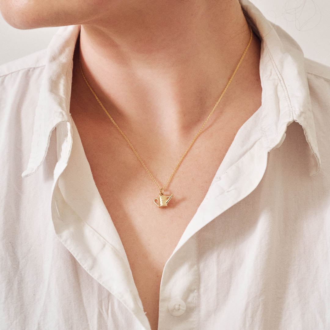 A miniature yellow gold watering can jewellery charm on a yellow gold rolo chain. Photographed being worn.