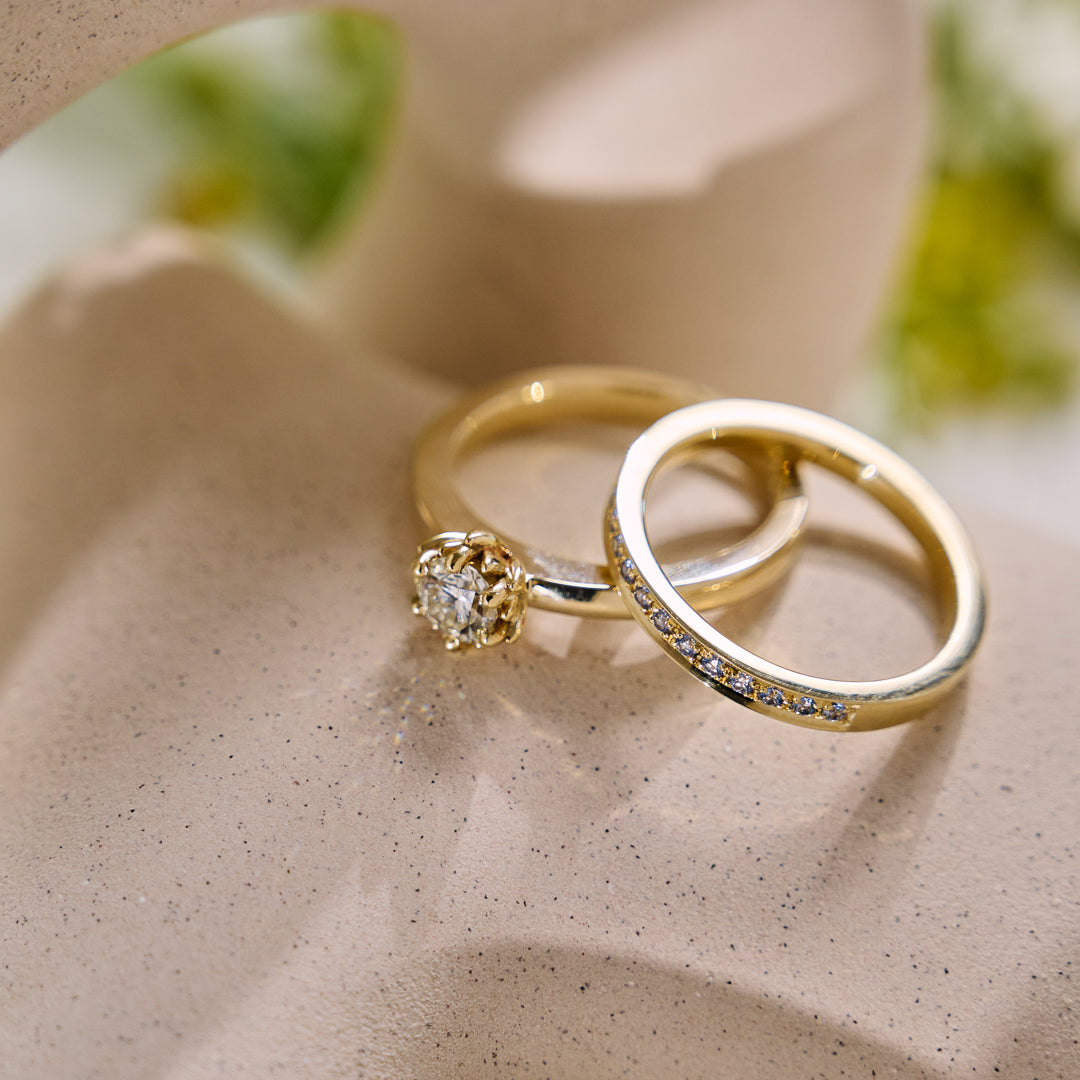 Two gold rings with diamond accents on a beige surface