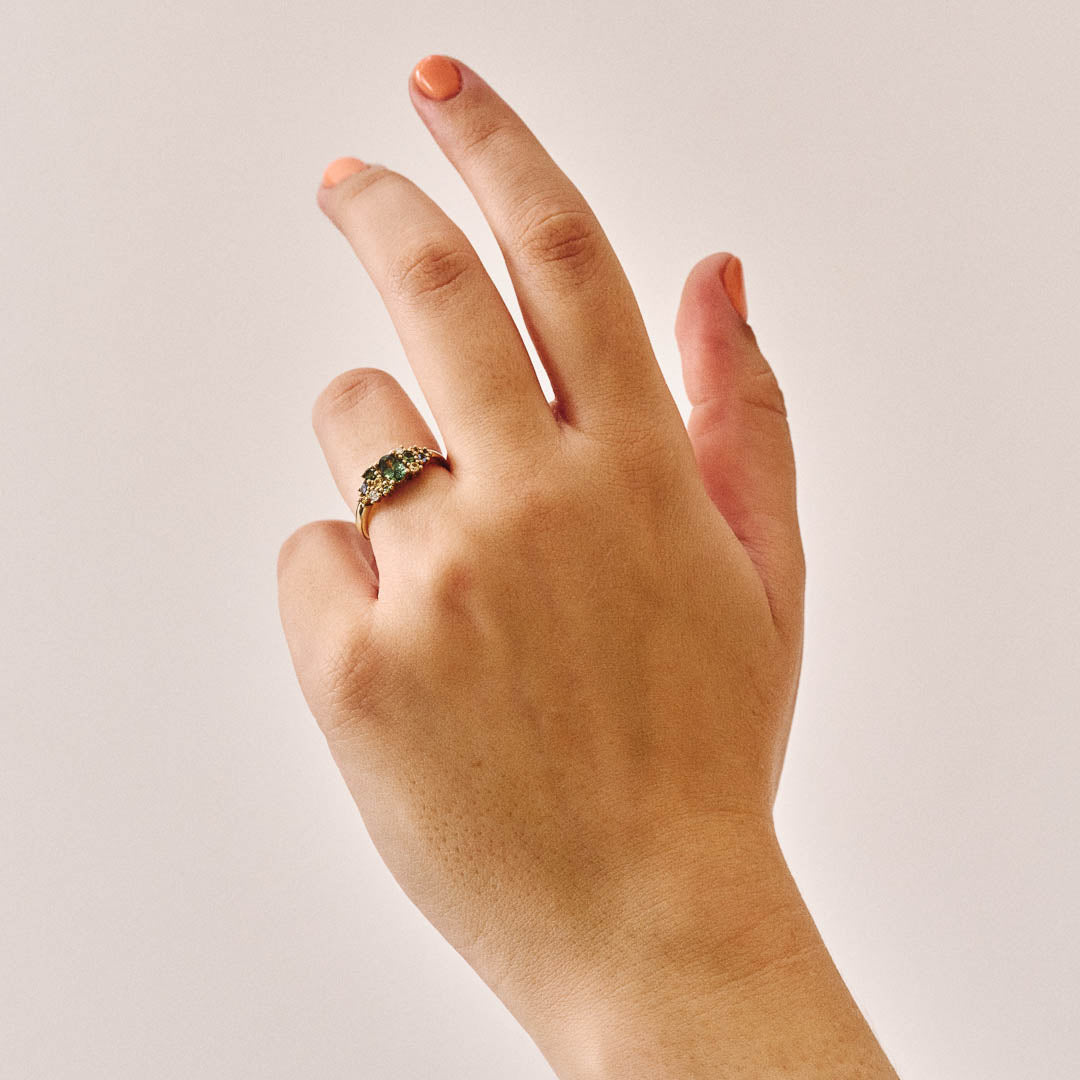 Unique handmade cluster engagement ring in 9ct yellow gold, featuring an oval green sapphire centre stone surrounded by a colourful bouquet-inspired mix of yellow, green, and blue sapphires with two natural diamonds.