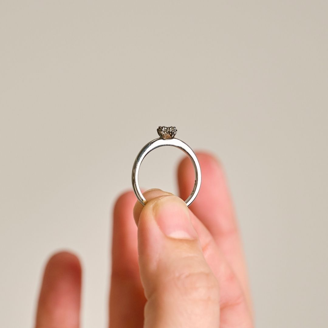 A platium protea ring held between two fingers to show the rings delicate proportions yet detailed protea petal setting. 