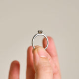 A platium protea ring held between two fingers to show the rings delicate proportions yet detailed protea petal setting. 