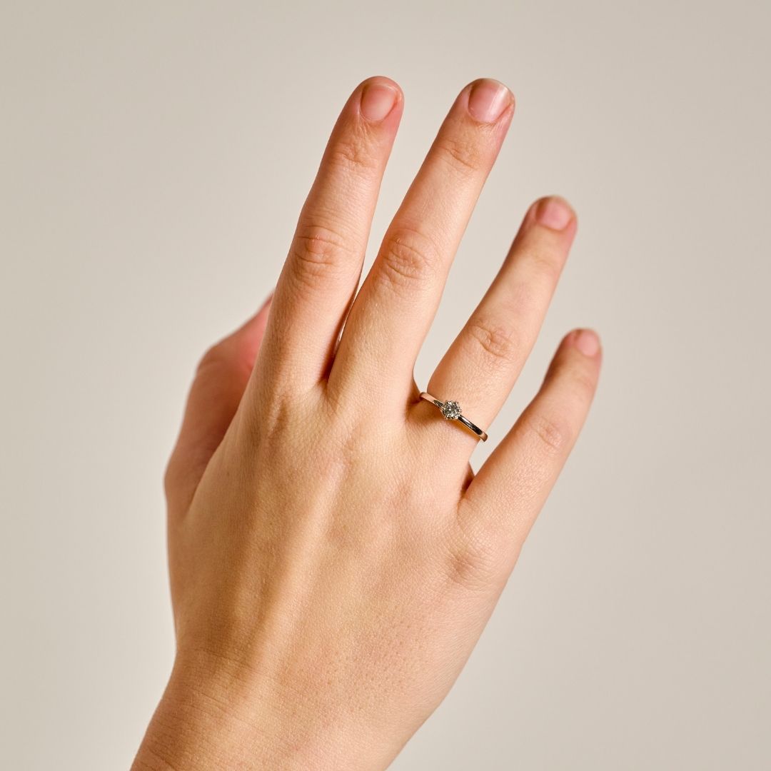 A close-up of a hand wearing Botanica platinum Petite Protea Ring with a small colourless natural diamond, set against a solid light beige background.
