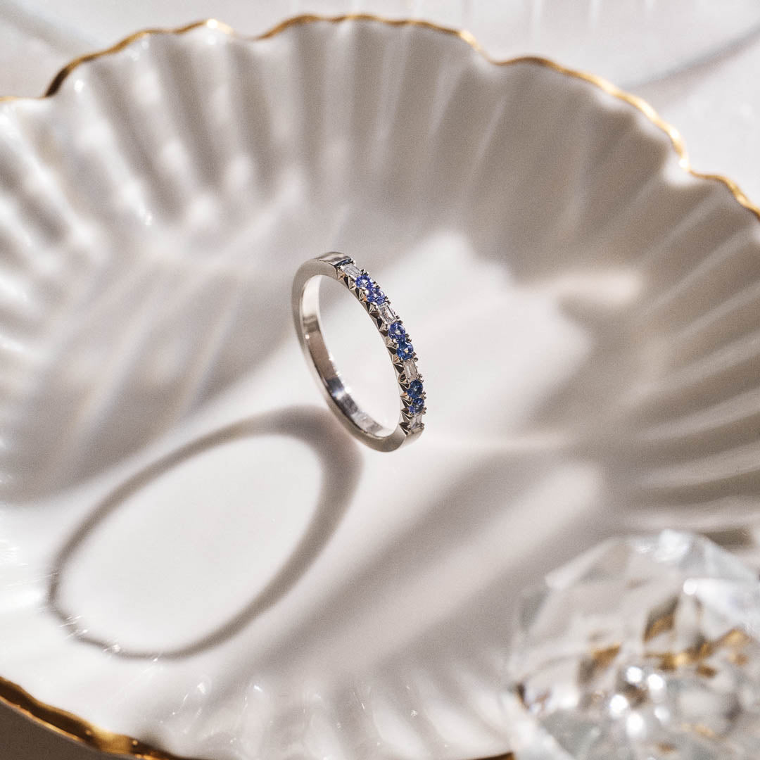 Luxury handmade platinum wedding ring featuring an intricate French pavé setting with baguette-cut natural diamonds and round light blue sapphires; a unique, high-end design perfect for weddings or milestone gifts.