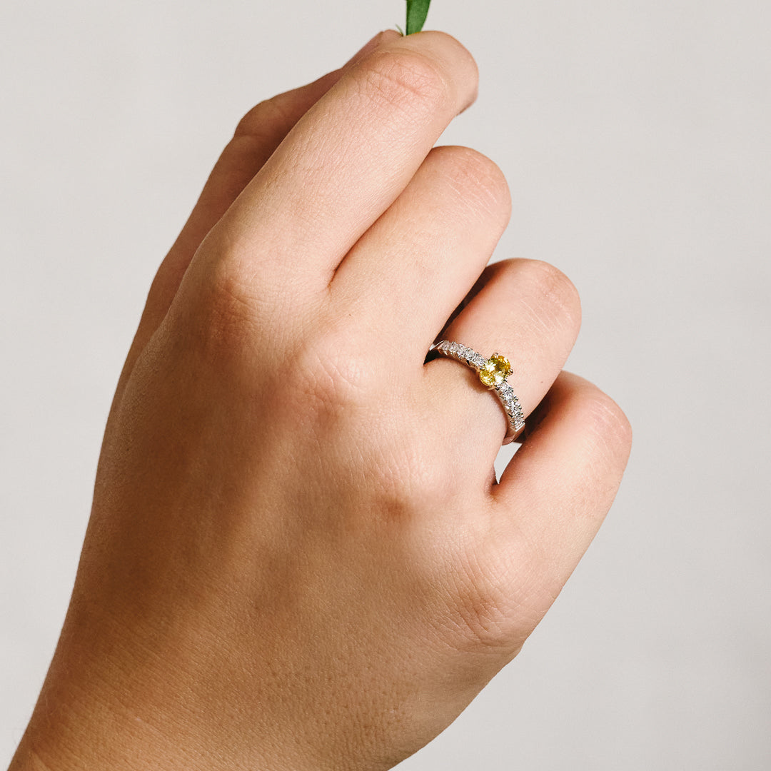 Hand wearing a platinum ring with central yellow sapphire set in yellow gold, and french pave natural diamonds.